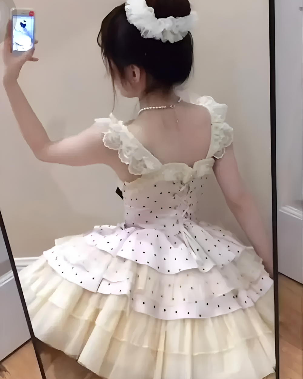 Woman wearing a white polka dot Hime Lolita dress with ruffled details, seen from the back in a mirror.