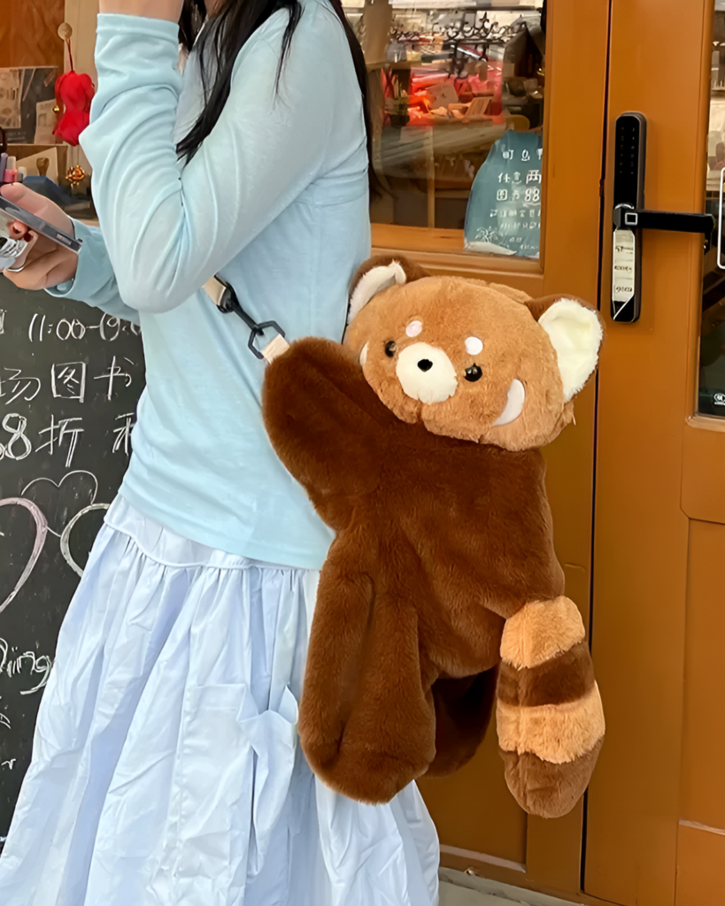 A brown Red Panda Plush Backpack is held by a person in an outdoor setting.
