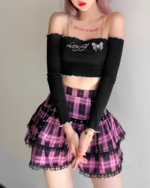 Model wearing a black top and a ruffled pink plaid mini skirt, embodying a mall goth aesthetic. Features a pink plaid mini skirt design.