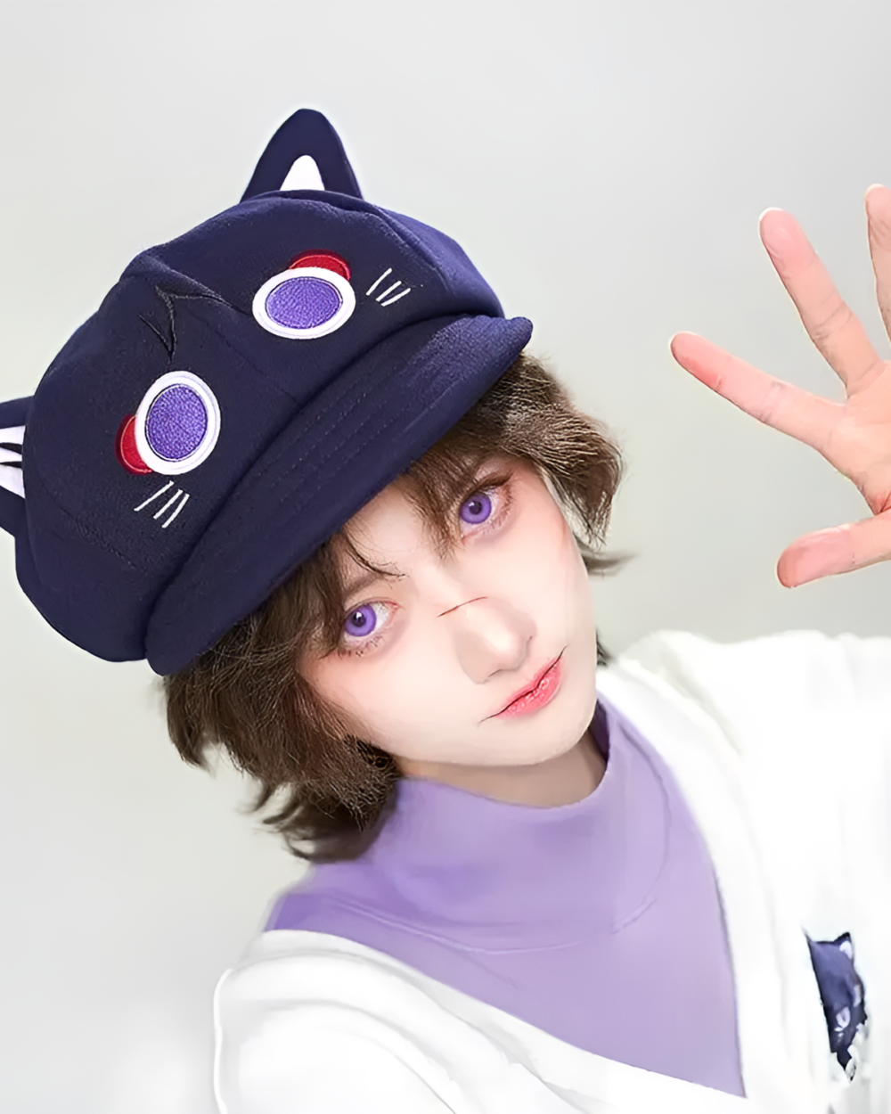 A person wearing a navy blue Scarameow Beret with cat ears and facial details. The beret features a white and red design.