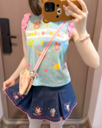 Girl wearing a blue sleeveless Mezzo Piano top with fruit & character prints, paired with a denim skirt.