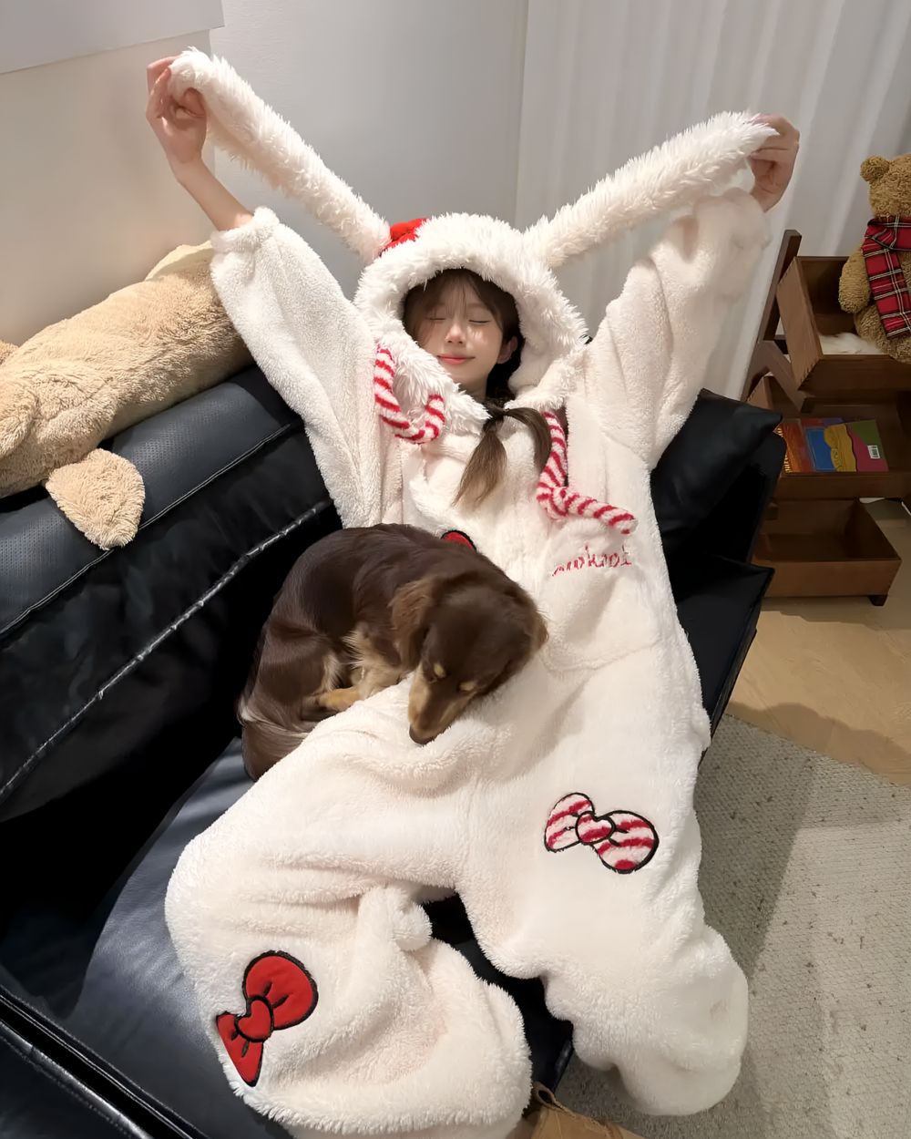 Woman wearing a white Slumber Bow-Bunny Ribbon Kigurumi Pajamas, a cozy bunny kigurumi, poses with a dog.
