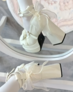 Image of white Starlit Lace-Bow Mary Janes with a lace bow and block heel, styled with stockings.