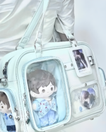 Light blue Strapped JK Ita Bag with clear window displaying collectible figures. Features adjustable straps and a cute design.