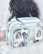 Woman wearing a light blue Strapped JK Ita Bag with clear pockets displaying photos and keychains.