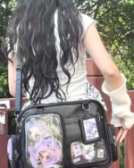 Woman wearing a white top and carrying a black Strapped JK Ita Bag with clear pockets displaying anime keychains.