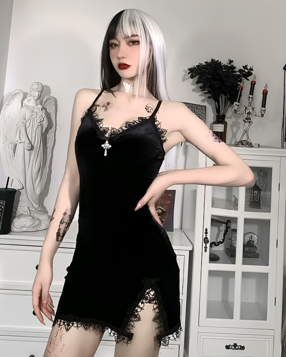 Woman modeling a black velvet goth mini dress with lace trim. The dress has spaghetti straps and a cross pendant.