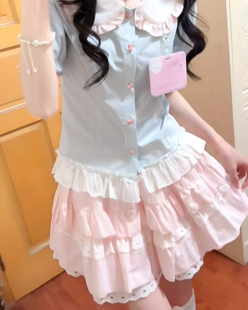 A person wearing a Sweet Lolita School Suit, featuring a light blue blouse and layered pink and white skirts.
