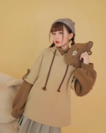 Model wearing a brown Bearcore hoodie with a plush teddy bear accessory and beanie.