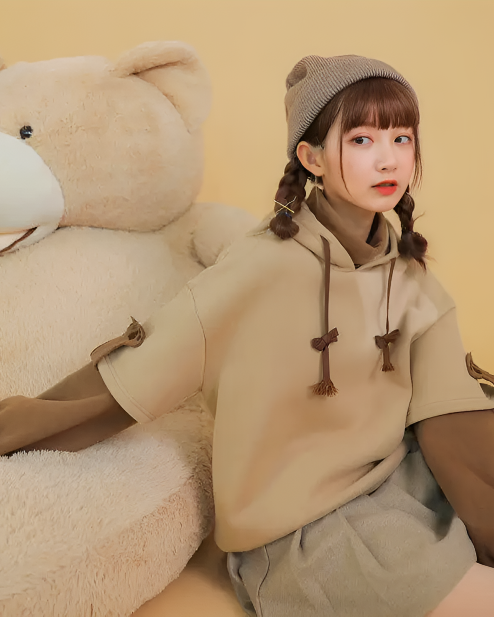 Model wearing The Bearcore hoodie with a teddy bear; beige casual style.