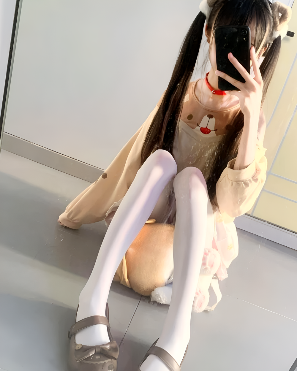 Woman holding a phone, showcasing a beige Doggy Sweatshirt with a bear design. She is wearing white tights and shoes.