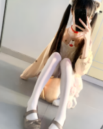 Woman holding a phone, showcasing a beige Doggy Sweatshirt with a bear design. She is wearing white tights and shoes.