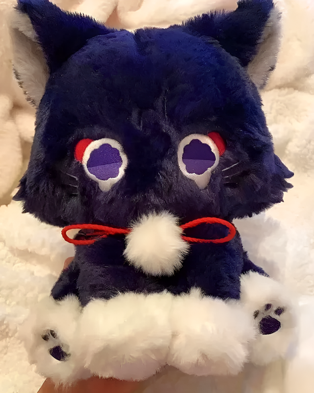 Close-up of the Scarameow plushie with dark blue fur, red eyes, and white paws. A detailed view of the Scarameow plushie’s face.