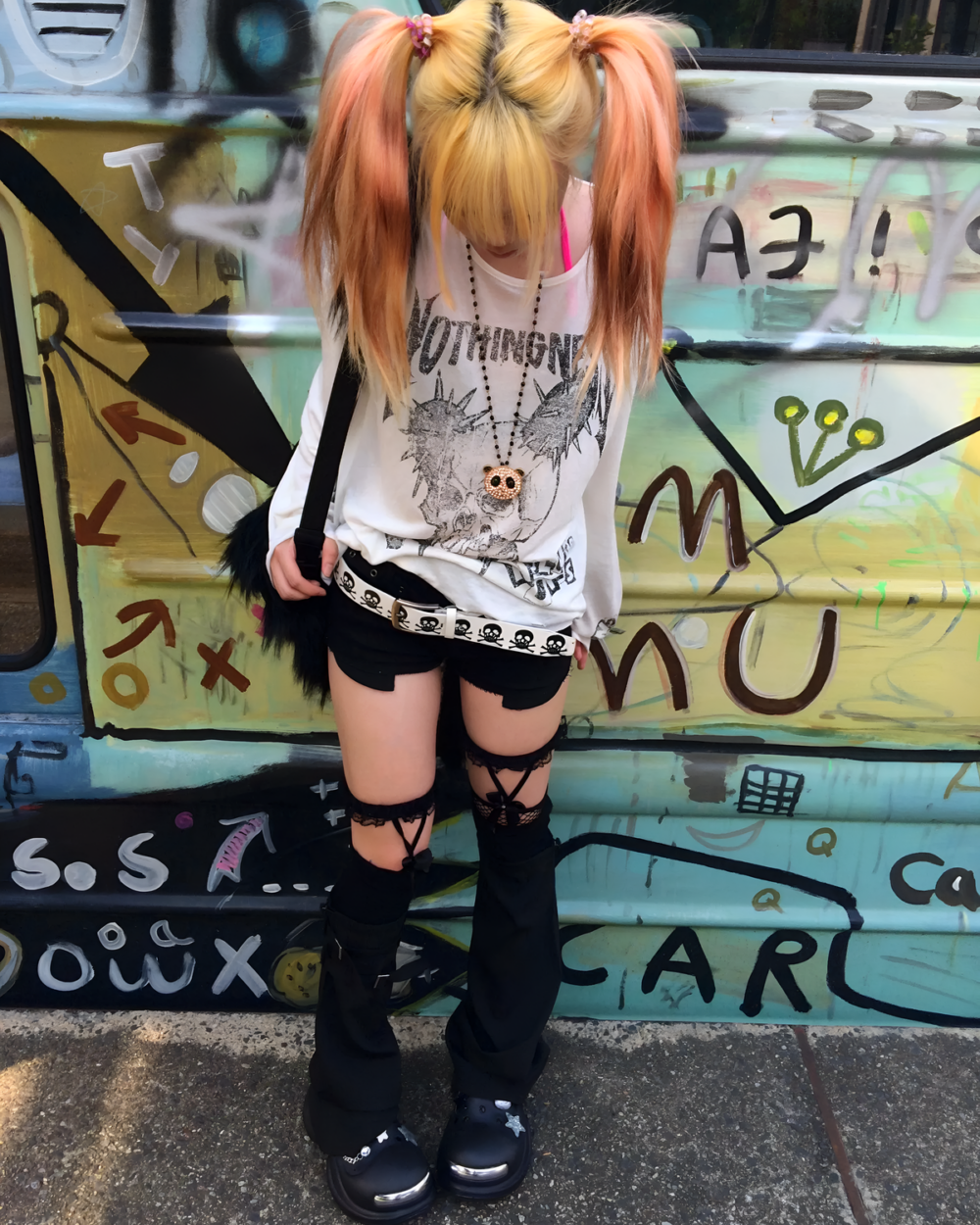 Person wearing a white Transluscent Nothingness T-Shirt with a skull graphic and black shorts in front of graffiti art.