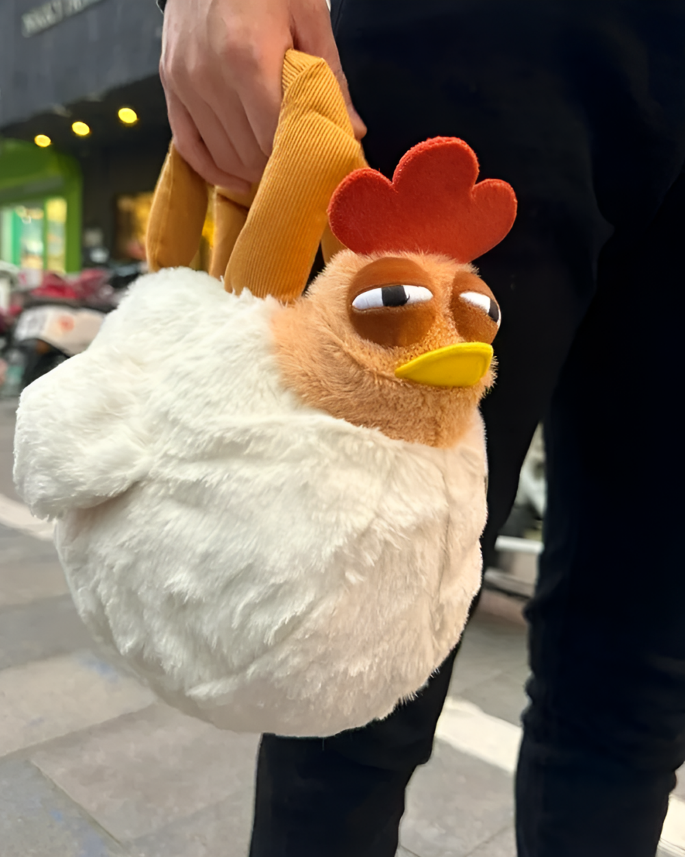 Ugly Chicken Plush Handbag product photo 1 Hand holding an unusual plush handbag shaped like an ugly chicken. The item is an ugly chicken plush handbag, with a red comb and yellow beak.