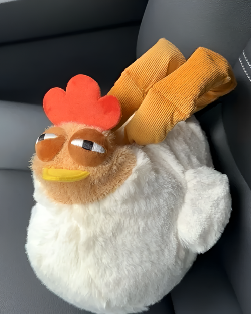 Close-up of an ugly chicken plush handbag with a red comb and yellow beak. The plush is white and fluffy.