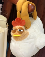 Close-up of an ugly chicken plush handbag with a red comb and yellow beak, displayed with other bags.