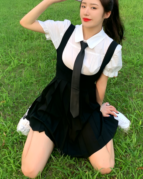 Woman wearing a black suspender skirt set with a white blouse and tie, styled with sneakers.