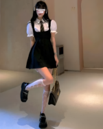 Woman wearing a black suspender skirt set with a white blouse and platform boots. Includes fishnet socks.