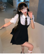 Woman wearing a black and white suspender skirt set with a blouse and tie. Includes lace trim and fishnet socks.