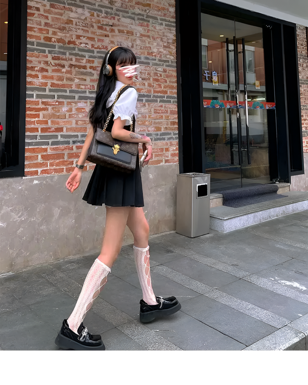Woman wearing a black suspender skirt set with a white blouse and knee-high socks.