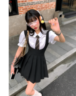 Woman wearing a black suspender skirt set with a white blouse and tie. The outfit includes suspenders and a pleated skirt.