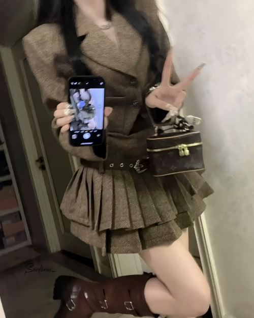 Model wearing a brown vintage pleated dress suit with a belt and handbag.