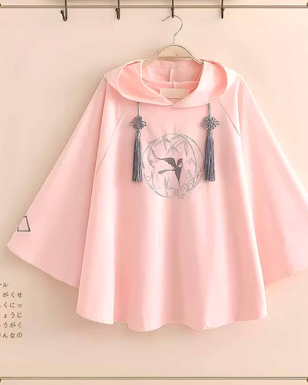 Pink Zephyr Bamboo hooded poncho with embroidery detail, hanging on a rack. A lightweight hooded poncho.