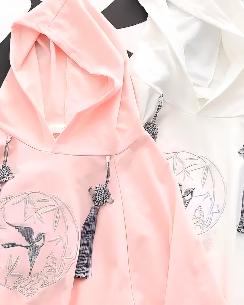 Close-up of Zephyr Bamboo hooded poncho in pink and white with embroidered bird details and tassel ties.