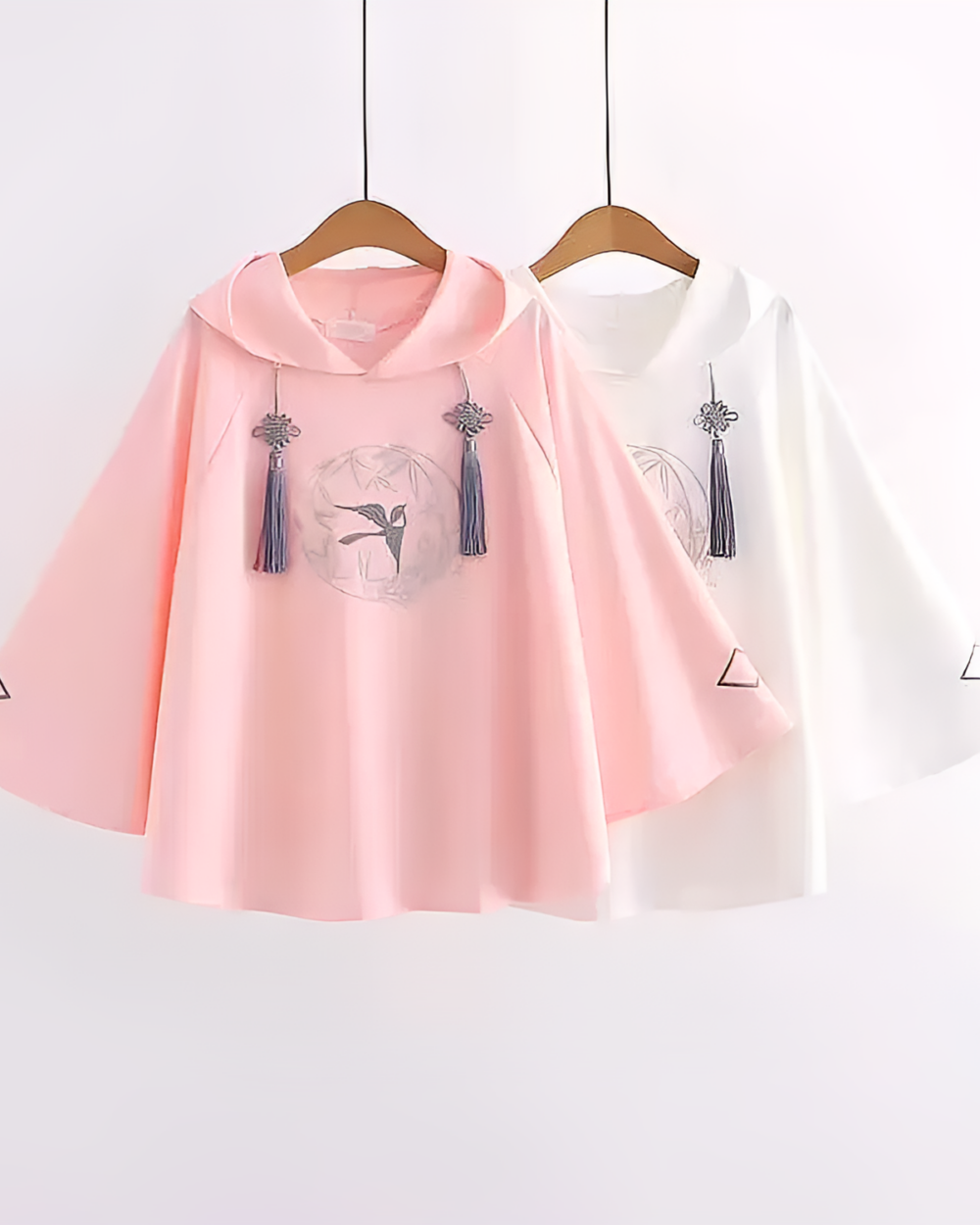 Pink and white Zephyr Bamboo hooded poncho with tassel details, hanging on a clothes rack.