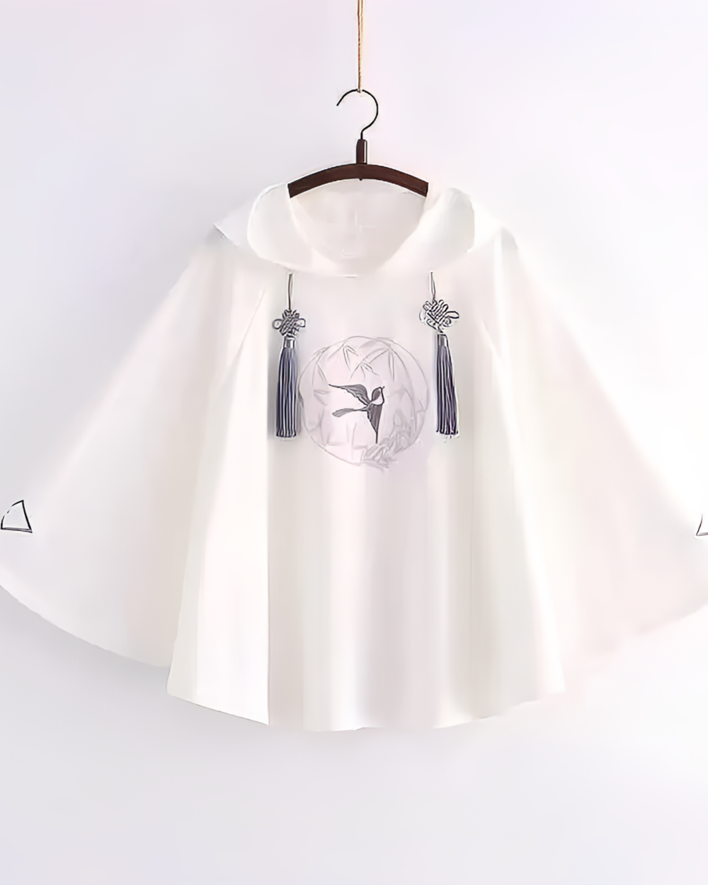 White Zephyr Bamboo hooded poncho with embroidered bird and tassel details, hanging on a wooden hanger.