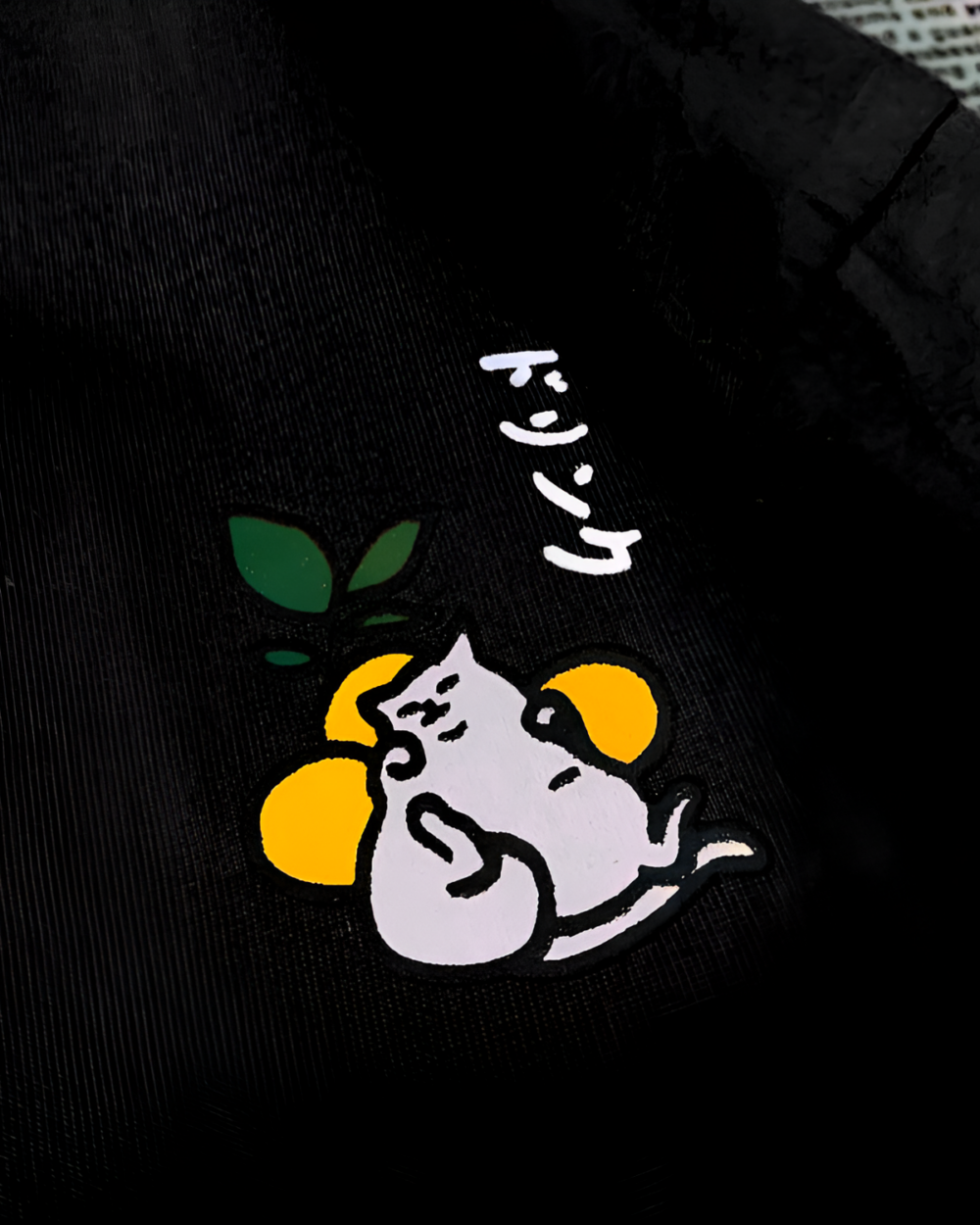 Close-up of a black t-shirt featuring a graphic of a white cat with oranges, a kawaii cat shirt design.